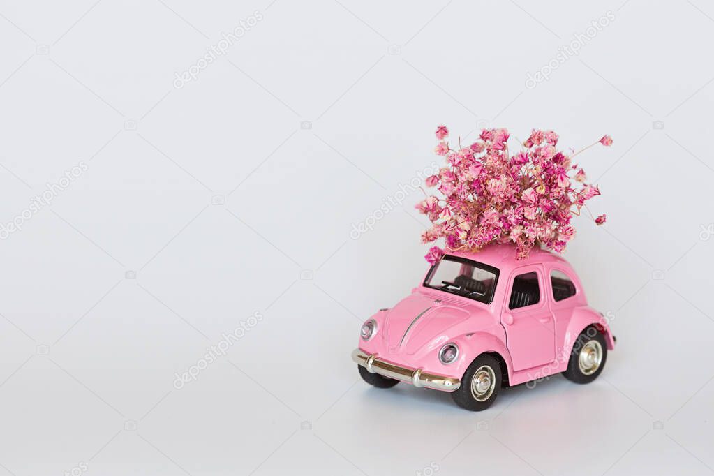 Changxing, China - October 15, 2019: Pink retro toy car delivering bouquet of flowers on white. Valentine day, February 14 card. International women day 8 March, mother day, birthday gift. Copy space,