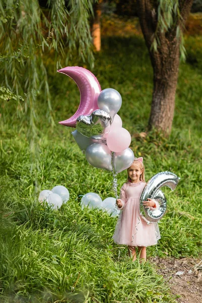 Außenaufnahmen von hübschen fröhlichen kleinen Mädchen mit blonden Haaren feiern 6 Jahre alten Geburtstag mit Luftballons, tragen modische Kleidung, haben aufgeregte Ausdrücke. Glückliche Kindheitserinnerungen — Stockfoto