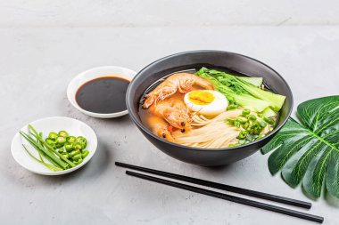 Asya erişte çorbası, karidesli ramen, sebze ve yumurta siyah kasede gri beton arka planda. Düz yatıyordu, Top view, model al, genel giderler. Sağlıklı gıda konsepti
