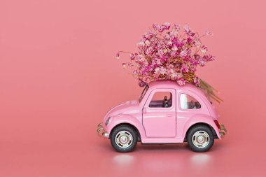 Changxing, Çin - 15 Ekim 2019: pembe arka planda çiçek buketi teslim eden pembe retro oyuncak araba. Sevgililer Günü, 14 Şubat kartı. Uluslararası Kadınlar Günü 8 Mart, Anneler Günü, Doğum günü hediyesi. C