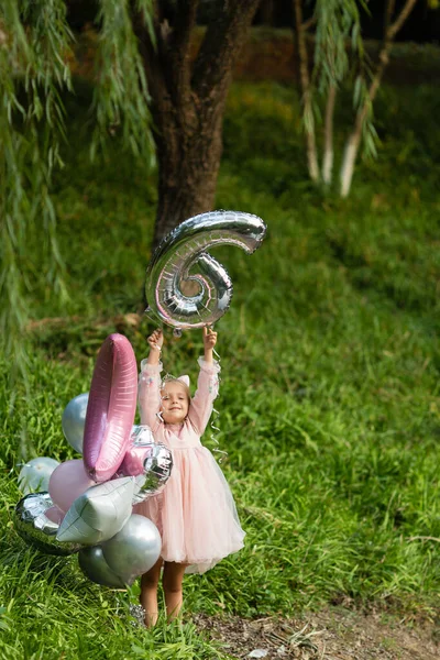Strzał na świeżym powietrzu dość radosne dziewczynki z blond włosami świętujące 6 lat urodziny z balonami, nosić modną sukienkę, mają ekscytujące wyrażenia. Szczęśliwe wspomnienia z dzieciństwa — Zdjęcie stockowe