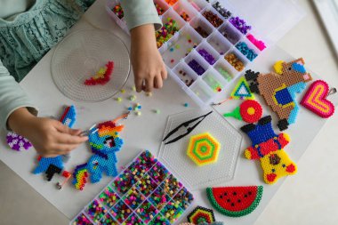 Şirin küçük kız termo mozaikle oyuncak yapıyor. Geliştirme, modellik, eğitim, sıcak plastikle tasarım. Modern teknolojiler. Diy..