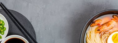 Asya erişte çorbası, karidesli ramen, sebze ve yumurta siyah kasede gri beton arka planda. Düz yatıyordu, Top view, model al, genel giderler. Sağlıklı gıda konsepti