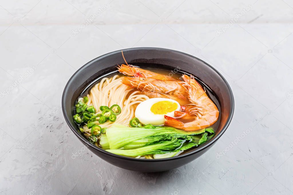 Asian noodle soup, ramen with prawn shrimp, vegetables and egg in black bowl on gray concrete background. Flat lay, Top view, mock up, overhead. Healthy food concept