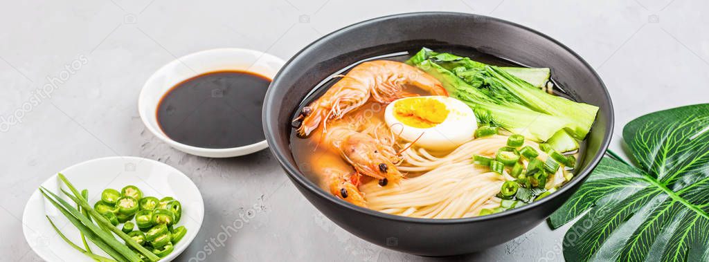 Asian noodle soup, ramen with prawn shrimp, vegetables and egg in black bowl on gray concrete background. Flat lay, Top view, mock up, overhead. Healthy food concept