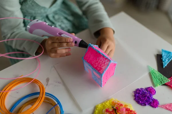 Şirin küçük kız plastik bir ev yapıyor, 3 boyutlu kalemle parçalar çiziyor. Kök ve Buhar Eğitimi. Geliştirme, modellik, eğitim, sıcak plastikle tasarım. Modern teknolojiler. Diy..