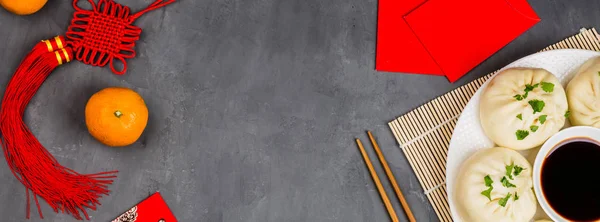 Chinese New Year decoration with dumplings, tangerines, soy sauce, chopsticks, red envelopes on gray concrete background. Happy Chinese new year 2020 festival