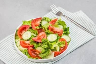 Masada sağlıklı vejetaryen yemeği, taze domatesli sebze salatası, salatalık, marul, gri beton arka planda kırmızı soğan. Diyet menüsü. Üst Manzara. Düz konum, model, kopyalama alanı olan şablon