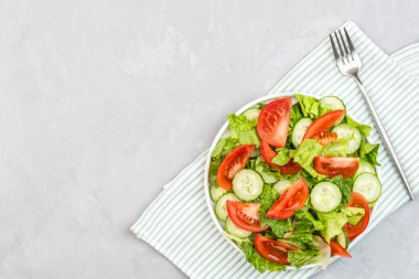 Masada sağlıklı vejetaryen yemeği, taze domatesli sebze salatası, salatalık, marul, gri beton arka planda kırmızı soğan. Diyet menüsü. Üst Manzara. Düz konum, model, kopyalama alanı olan şablon