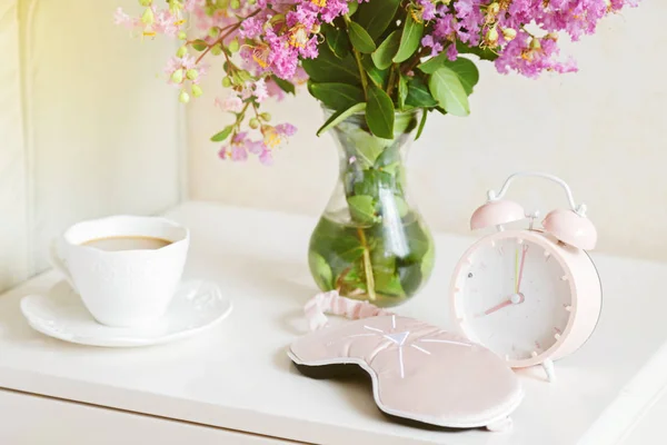 闹钟的特写，一杯咖啡和一束粉红色的花朵，背景在晨曦中 — 图库照片