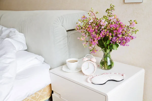 Réveil gros plan, une tasse de café et un bouquet de fleurs roses fond dans la lumière du soleil du matin — Photo