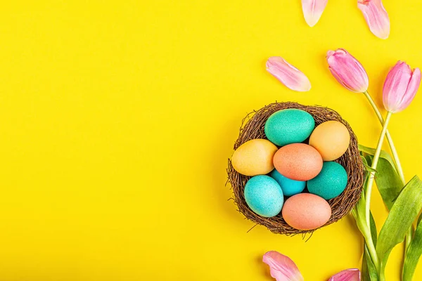 Κομψό φόντο με πολύχρωμα πασχαλινά αυγά απομονωμένα σε κίτρινο φόντο με ροζ λουλούδια τουλίπας. Επίπεδη lay, κορυφαία άποψη, mockup, γενικά, πρότυπο — Φωτογραφία Αρχείου