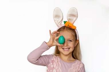Beyaz arka planda izole edilmiş Paskalya yumurtası tutan tavşan kulaklı şirin bir kız. Sevimli çocuk Paskalya bayramını kutluyor