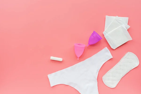 Copa menstrual con bolsa, almohadillas higiénicas, tampón, bragas blancas sobre fondo rosa. Producto alternativo de higiene femenina durante el período. Concepto de salud femenina . — Foto de Stock