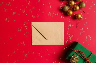 Noel kompozisyonu. Zarf, paket hediye, kırmızı arka planda altın konfetili oyuncaklar. Yeni yıl konsepti. Kutlama kartı, xmas kutlaması 2020. Düz konum, üst görünüm, kopyalama alanı, modelleme