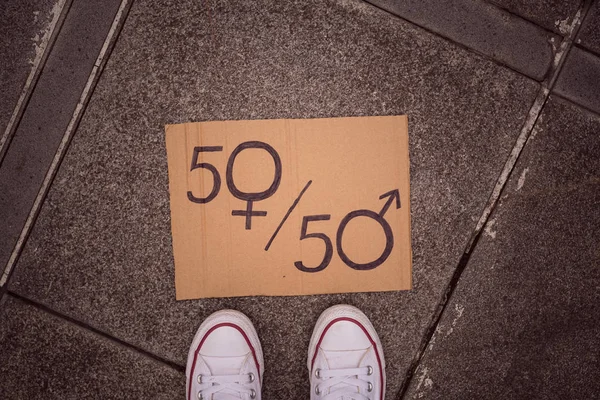 混雑した街路の背景の上に男性と女性のシンボルを持つ女性の脚と紙シートとしての男女平等の概念。屋外で抗議する女性社会問題のメタファーとしてのセックスサイン。上のビュー、フラット — ストック写真