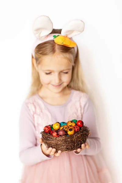 Niña linda sosteniendo nido con huevos de Pascua sobre fondo blanco. Adorable niño celebrar vacaciones de Pascua — Foto de Stock