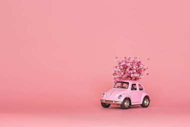 Changxing, Çin - 15 Ekim 2019: pembe arka planda çiçek buketi teslim eden pembe retro oyuncak araba. Sevgililer Günü, 14 Şubat kartı. Uluslararası Kadınlar Günü 8 Mart, Anneler Günü, Doğum günü hediyesi. Boşluğu kopyala, modelle, şablonu en aza indir