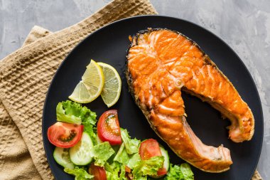 Kızarmış somon balığı bifteği, sebze salatası ve siyah tabakta limon. Balıktan, maruldan, domatesten, salatalıktan, salatalıktan, üst manzaradan, düz yataktan, maketten, genel masraftan oluşan yaratıcı bir düzen. Sağlıklı gıda konsepti