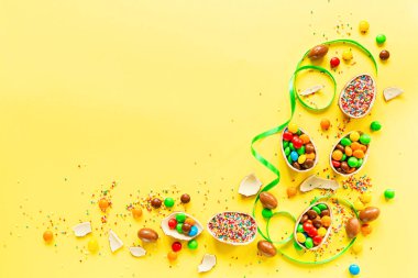 Çikolatalı Paskalya yumurtası ve sarı kağıtta renkli şekerler. düz konum, kopyalama alanı, üst görünüm, genel görünüm, şablon, modelleme.