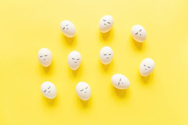 Tatlı yüzlü yaratıcı paskalya yumurtaları ve pastel sarısı arka planda uykulu gözler. Mutlu Paskalyalar. Düz konum, üst görünüm, model, şablon, genel görünüm, boşluğu kopyala.