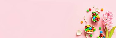 Çikolatalı Paskalya yumurtası ve pastel pembe kağıtta renkli şekerler. Düz konum, üst görünüm, üstten görünüm, kopyalama alanı, şablon, model. Web tasarımı için yatay pankart.