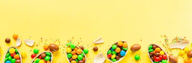 Çikolatalı Paskalya yumurtası ve sarı kağıtta renkli şekerler. düz konum, kopyalama alanı, üst görünüm, genel görünüm, şablon, modelleme.