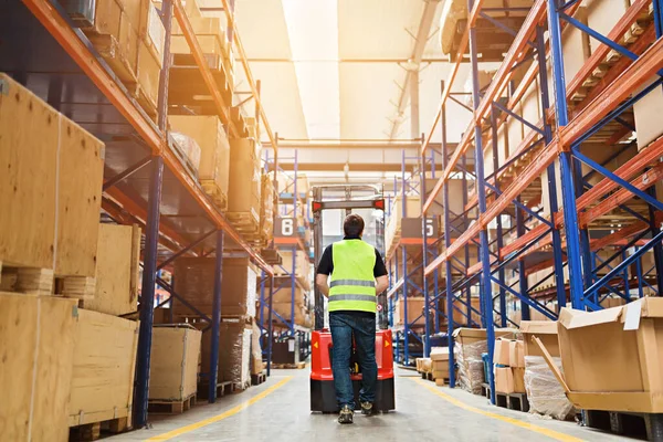 Depo çalışanı üniformalı bir forklift kullanıyor ve modern otomatik depoda kutuları var. Kutular deponun raflarında. Depo, makine konsepti. Stokta lojistik.