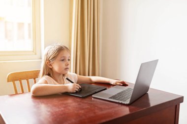 Evdeki online dersi sırasında ödev okuyan güzel bir liseli kız, karantina sırasındaki sosyal mesafe, kendini izole etme, çevrimiçi eğitim konsepti, evde eğitim veren. Oturma odasındaki işyeri