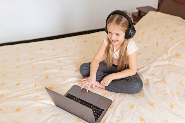 Stay at home quarantine coronavirus pandemic prevention. Little girl with blonde hair sitting on the bed and using laptop. Prevention epidemic. Child using technology