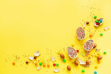 Çikolatalı Paskalya yumurtası ve sarı kağıtta renkli şekerler. düz konum, kopyalama alanı, üst görünüm, genel görünüm, şablon, modelleme.