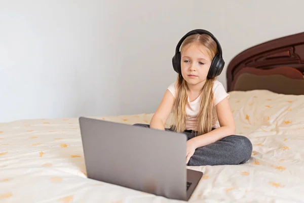 Stay at home quarantine coronavirus pandemic prevention. Little girl with blonde hair sitting on the bed and using laptop. Prevention epidemic. Child using technology