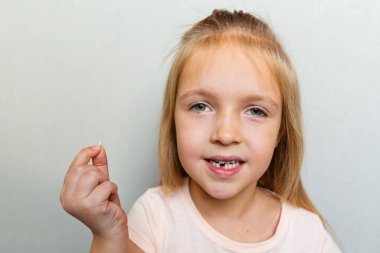İlk süt dişini gösteren çocuk. Diş konseptini değiştir. Gri arkaplanda sarı saçlı ve fotokopi alanı olan tatlı küçük kız.