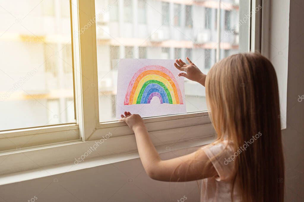 Kid painting rainbow during Covid-19 quarantine at home. Stay at home Social media campaign for coronavirus prevention, let's all be well, hope during coronavirus pandemic concept.