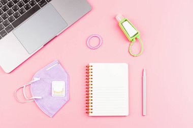 Dizüstü bilgisayarlı Çalışma Alanı Masası, Boş Not Defteri, Pembe arka planda Tıbbi Maske. Düz döşeme, kopyalama alanı, model, şablon. Evden çalışıyor, salgın sırasında evde kalıyor ve karantina altında.