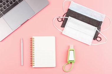 Bilgisayarlı Çalışma Alanı Masası, Boş Not Defteri, Pembe arka planda Tıbbi Maskeler. Düz döşeme, kopyalama alanı, model, şablon. Evden çalışıyor, salgın sırasında evde kalıyor ve karantina altında.