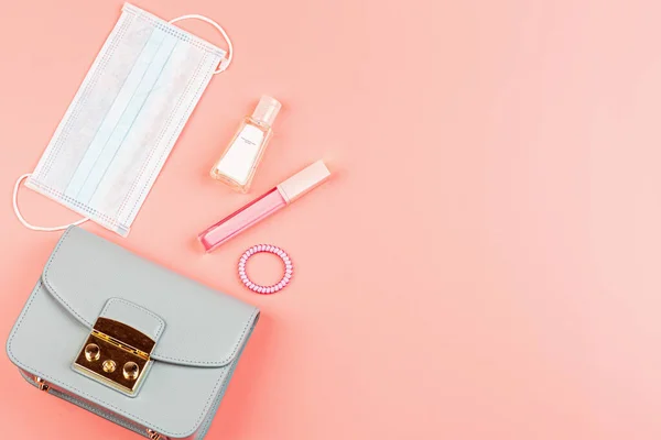 Flat lay of leather woman bag open out with face mask, sanitizer hand gel to protect from Coronavirus or COVID-19, lipstick, accessories on pink background with copy space — Stock Photo, Image