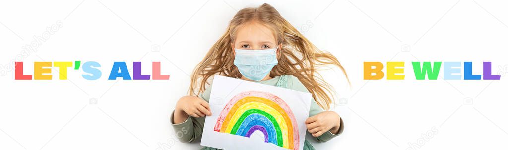 Little girl in mask holding painted rainbow during Covid-19 quarantine. Stay at home Social media campaign for coronavirus prevention, lets all be well, hope during coronavirus pandemic concept