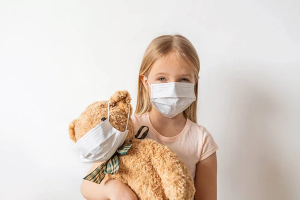 Coronavirus ve Hava kirliliği pm2.5 konsepti. Karantina sırasında oyuncak ayısını korumak ve tutmak için maske takan küçük Rus kız. Önleme salgını. Yurt içi kampanyada kal .