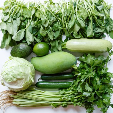 Düz yiyecek, taze yeşil sebze ve meyveler: kereviz, salatalık, mango, limon, lahana, beyaz mutfak masasında ıspanak. Üst Manzara. Coronavirus covid-19 kilitlenmesi sırasında sağlıklı yaşam tarzı ve diyet.
