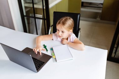 Evdeki online dersi sırasında ödev okuyan güzel bir liseli kız, karantina sırasındaki sosyal mesafe, kendini izole etme, çevrimiçi eğitim konsepti, evde eğitim veren. Oturma odasındaki işyeri
