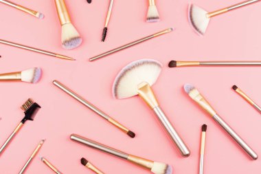 Pembe arka planda farklı makyaj fırçaları. Düz yerde, üst tarafta. Makyaj aksesuarları, maket, şablon. Dergiler ve sosyal medya için kompozisyon.