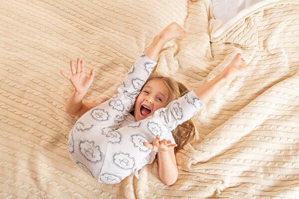 Beautiful little girl in pajamas jumping on the bed at home. Stay at home during coronavirus covid-19 lockdown and have a fun.