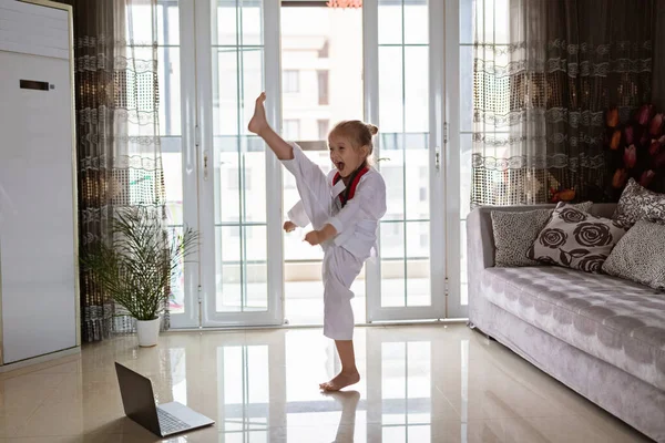 Taekwondo ragazza in kimono con cintura bianca che si esercita a casa in soggiorno. Educazione online durante il coronavirus covid-19 isolamento, auto isolamento e concetto di distanza sociale — Foto Stock