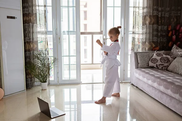 Taekwondo ragazza in kimono con cintura bianca che si esercita a casa in soggiorno. Educazione online durante il coronavirus covid-19 isolamento, auto isolamento e concetto di distanza sociale — Foto Stock