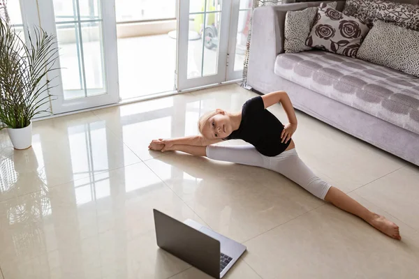 Cute little girl in sportswear watching online video on laptop and doing fitness exercises at home. Distant training with personal trainer, social distance or self-isolation, online education concept.