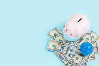 Domuz kumbarası ve nakit para mavi arka planda 100 dolarlık banknotlar. Düz yatış, üst görünüm, genel görünüş, model, şablon. Coronavirus covid-19 salgını sonrası mali kriz kavramı.