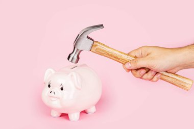 Erkeklerin eli çekiç kumbarasıyla pembe arka planda eziliyor. Model, şablon. Coronavirüs covid-19 salgınından sonraki finansal kriz kavramı.