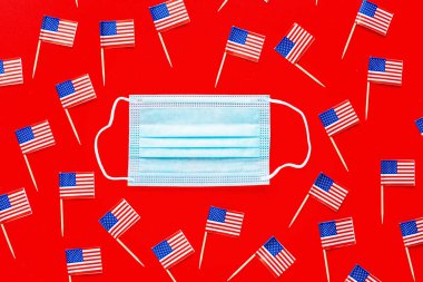 4 Temmuz. Kırmızı arka planda ABD bayrakları ve tıbbi maske. Amerika 'nın Bağımsızlık Günü 2020 Coronavirus covid-19 pandemik karantinası sırasında. Düz konum, üst görünüm, şablon.