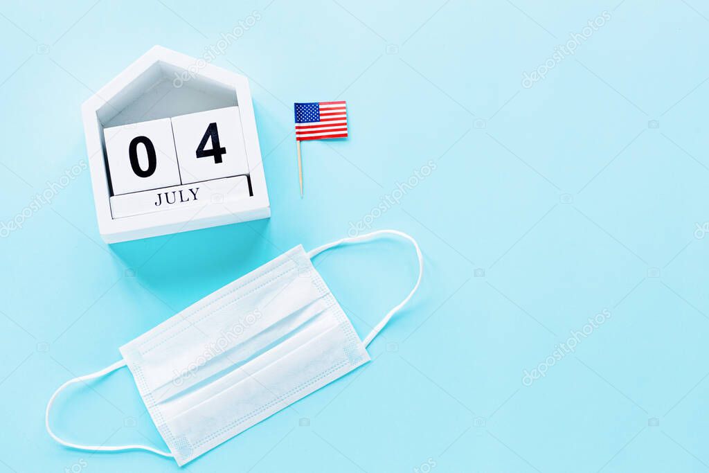 July 4th. USA flag and medical mask on blue background. Independence Day Of America 2020 during coronavirus covid-19 pandemic quarantine. Flat lay, top view, template.